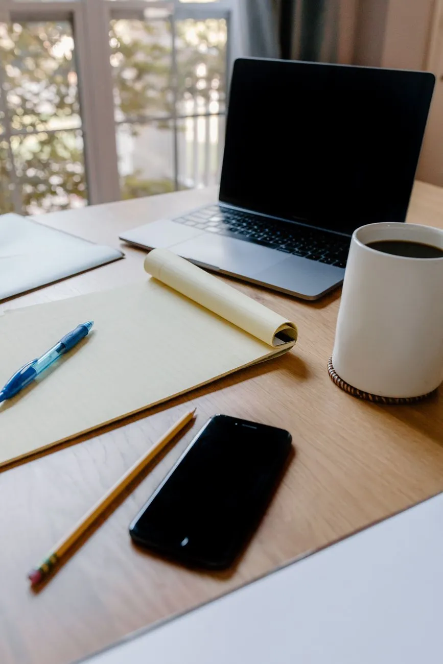 A cozy home office scene with a laptop, notebook, smartphone, and coffee, perfect for productivity.