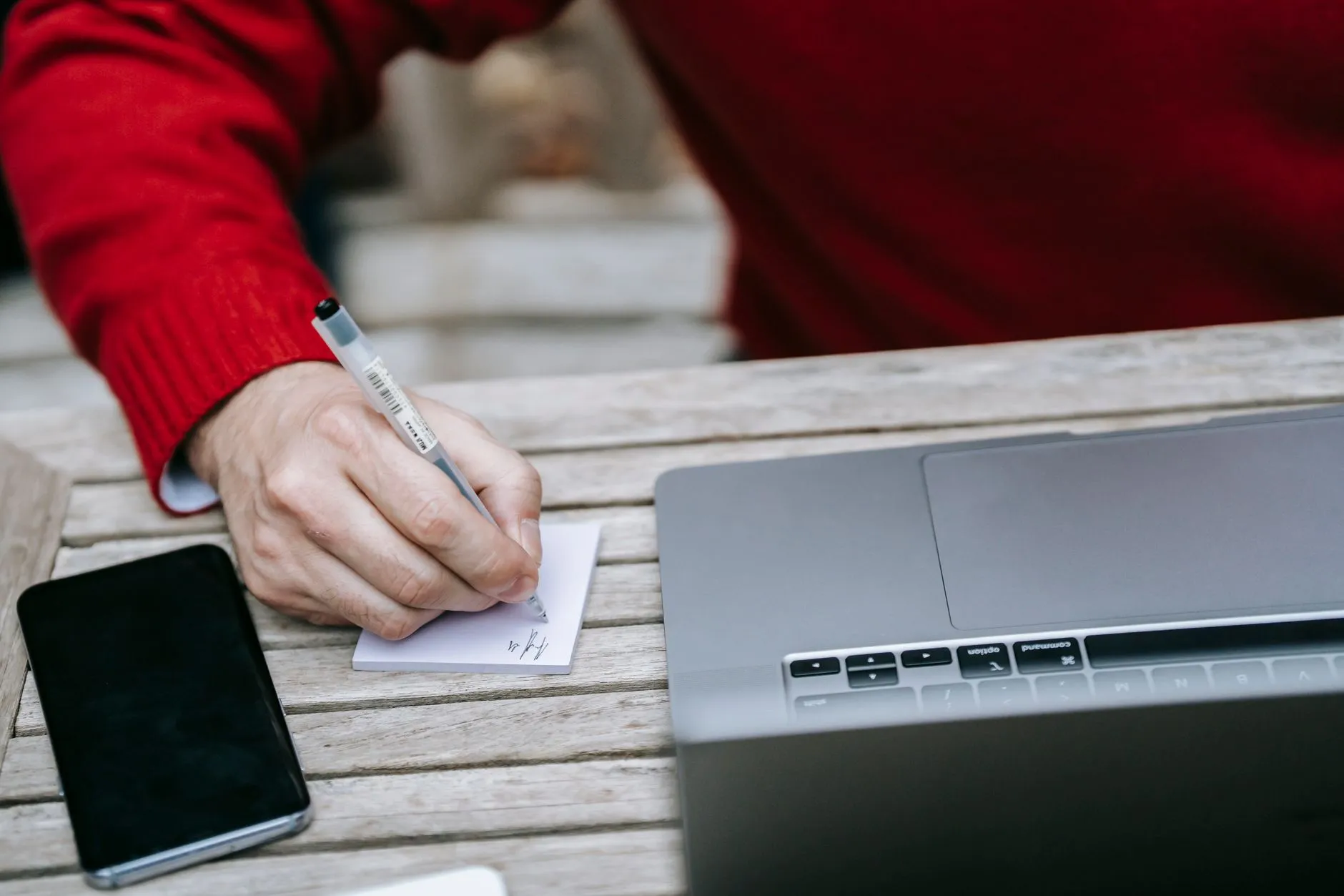 Individual working on a laptop and writing notes on a red table outdoors.