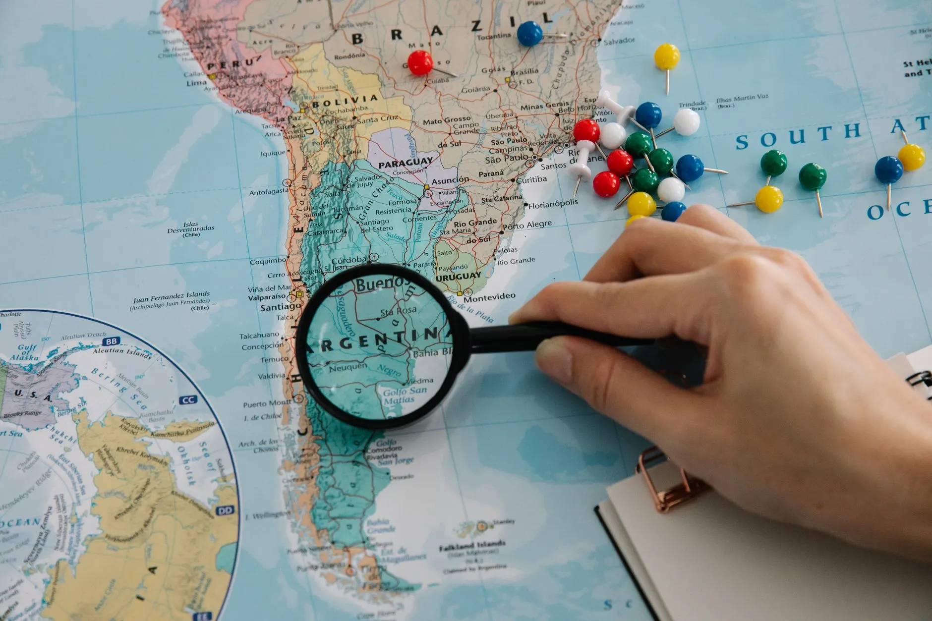 Magnifying glass focuses on pins highlighting travel destinations on a world map.