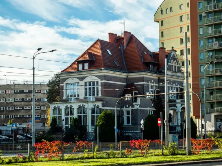 Beautiful old house with red roof surrounded by modern city buildings.