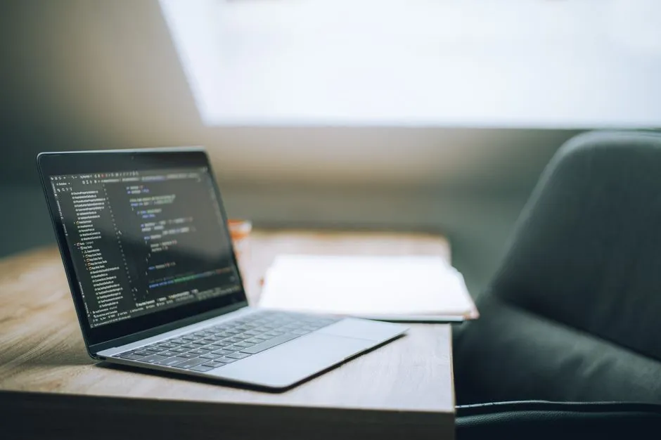 Open laptop displaying code on desk in bright, modern office setting. Ideal for tech and remote work context.