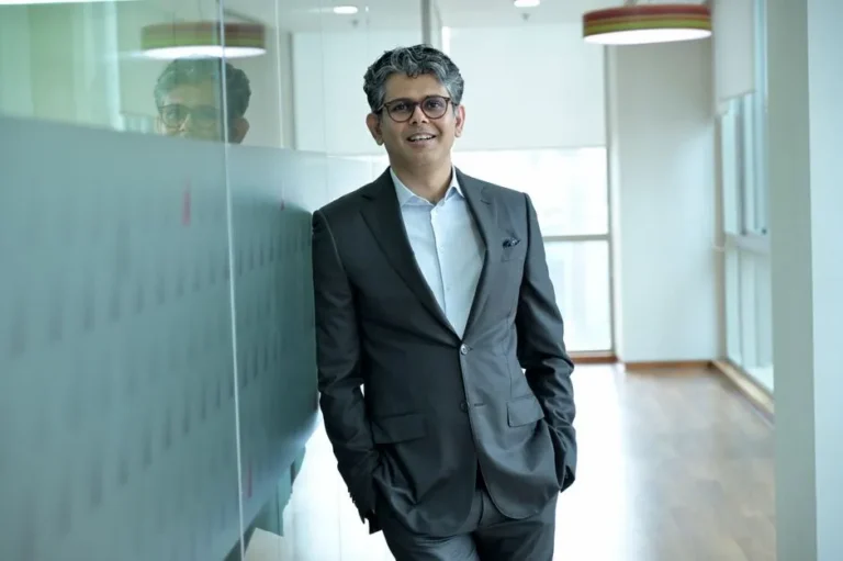 Smiling businessman standing confidently in a modern office hallway, wearing a suit.